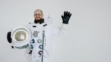 Elinde miğfer olan astronot diğer eliyle arka planda hafif dalgalar yaratıyor.