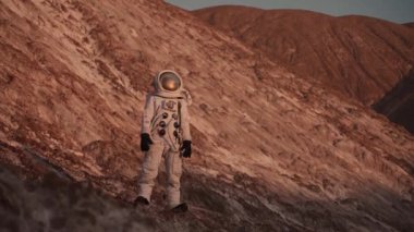  Bir astronot kayanın üzerinde durur ve mesafeye bakar. Kamera ona doğru hareket eder.