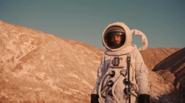  Tepelerdeki astronot elini kaldırdı ve parlak güneşten uzaklaştı.