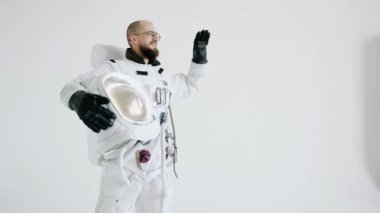 Elinde miğfer olan astronot diğer eliyle arka planda hafif dalgalar yaratıyor.