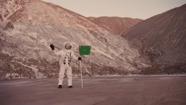 Astronauta na tle wzgórz z flagą machającą ręką — Wideo stockowe