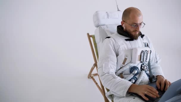 メガネをかけた宇宙飛行士が椅子に座ってノートパソコンを膝の上に置きます。スタジオ — ストック動画