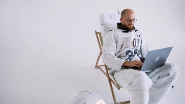 Astronauta con gafas se sienta en una silla trabaja con un ordenador portátil en su regazo. estudio — Vídeos de Stock