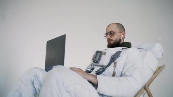 Astronautul cu ochelari stă într-un scaun și lucrează cu un laptop în poală. studio — Videoclip de stoc