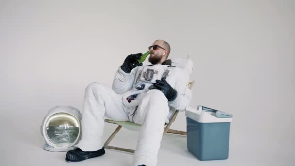 Astronauta se sienta en una silla con un teléfono en la mano y escucha música. estudio — Vídeos de Stock