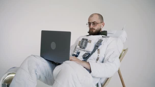 Astronauta con gafas se sienta en una silla trabaja con un ordenador portátil en su regazo. estudio — Vídeos de Stock