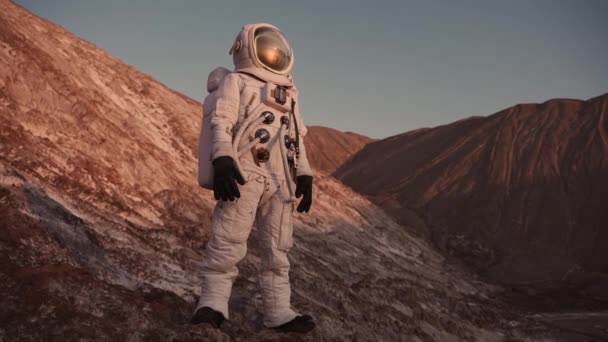 岩の上に立つ宇宙飛行士はヘルメットのフラップを開けて周りを見回し — ストック動画