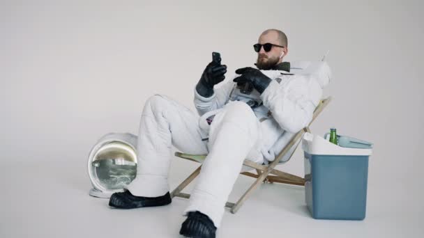 Astronauta senta-se em uma cadeira com um telefone na mão e ouve música. estúdio — Vídeo de Stock