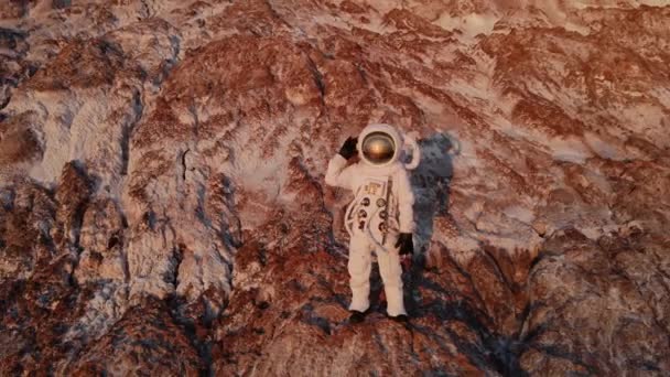 Astronauta stojący na skale machający ręką. zdjęcia lotnicze — Wideo stockowe