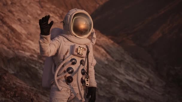 Astronot bir kaya üzerinde durup el sallıyor ve baş parmağını kaldırıyor. Güneş parlıyor. — Stok video