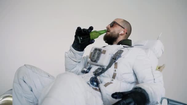Astronauta siedzi na krześle z butelką w ręku i pije. studio — Wideo stockowe
