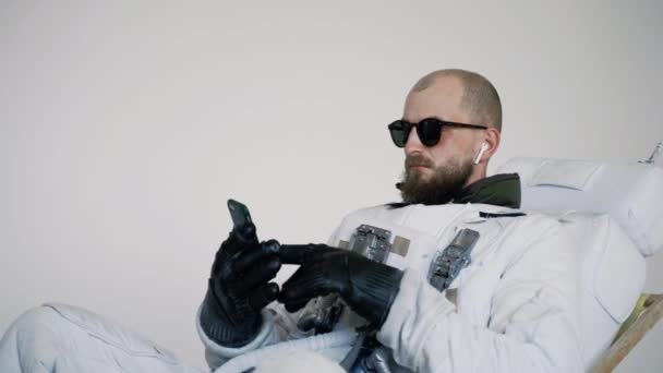 Astronaute s'assoit sur une chaise avec un téléphone à la main et écoute de la musique. studio — Video