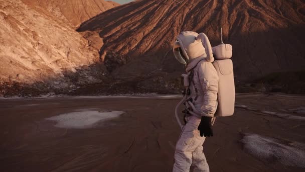 O astronauta caminha cautelosamente contra o pano de fundo das colinas — Vídeo de Stock