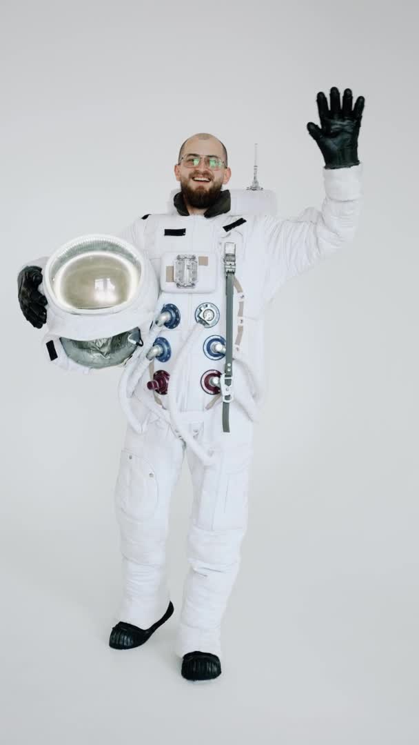 Astronaut with helmet in his hand on light background waves with his other hand — Stock Video