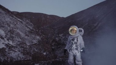 Alacakaranlıkta elinde fenerle bir astronot tepeden aşağı doğru buhar bulutu içinde yürüyor.