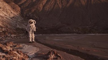 Astronot akarsu boyunca dikkatlice yürür ve elini kaldırır.. 