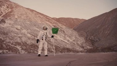  Tepelerin yanındaki astronot miğferin bölünmesini kapatıyor.