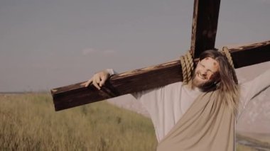 İsa haçı sırtında taşıyor. Çimlerin üzerinde yürür, tepelerin arkasında. 