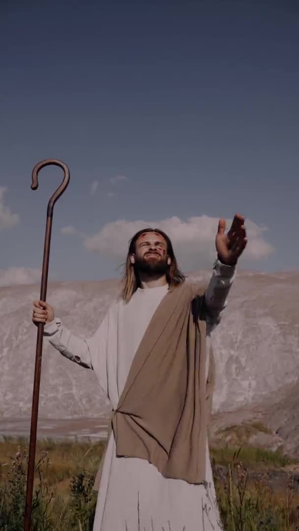 Jesus ergue-se contra montanhas levantando a mão olhando para o céu. Vertical — Vídeo de Stock