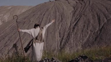 İsa dağlara karşı duruyor ellerini kaldırıp gökyüzüne bakıyor ve bağırıyor.