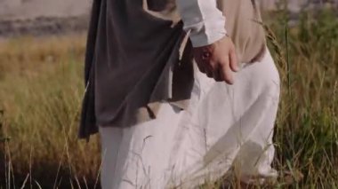 İsa çimlerin üzerinde yürüyor, elleriyle kulaklara dokunuyor. Yakın plan..