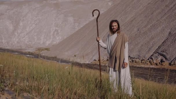 イエス・キリストは衣を着たスタッフとともに山の上に立って遠くを見ています. — ストック動画