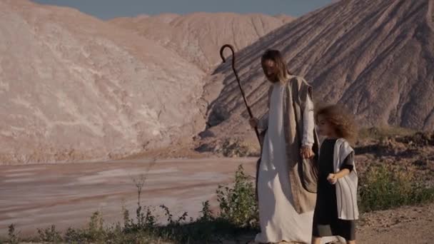 Jesús camina con la niña sosteniendo su mano hacia el embalse. El sol brilla — Vídeo de stock