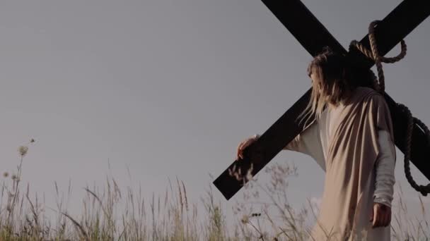 Jesús está de pie con una cruz sobre sus hombros. El viento sopla. La hierba se balancea — Vídeo de stock
