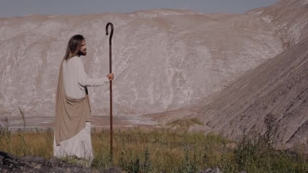 Jézus Krisztus egy bottal a köntösben áll a hegyen, és keres messze. — Stock videók