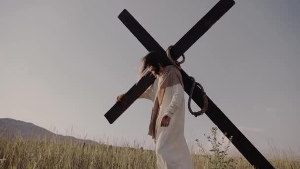 Jesus carries the cross on his back. walks on the grass, background of hills. — Stock Video