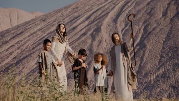 イエスとメアリーは遠くの子供たちに何かを示す丘の上に立っています — ストック動画