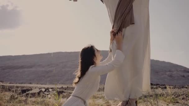 Maria cai aos pés de Jesus e chora a sua morte. O vento está soprando. — Vídeo de Stock