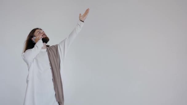 Jesus speaks on the phone raising his hand, looking up. On white background. — Stock Video