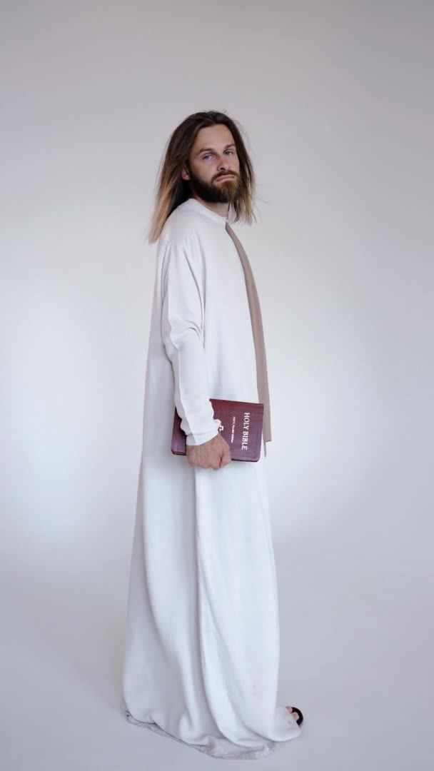 Jezus kijkt in de camera en houdt de Bijbel in zijn handen op een witte achtergrond — Stockvideo