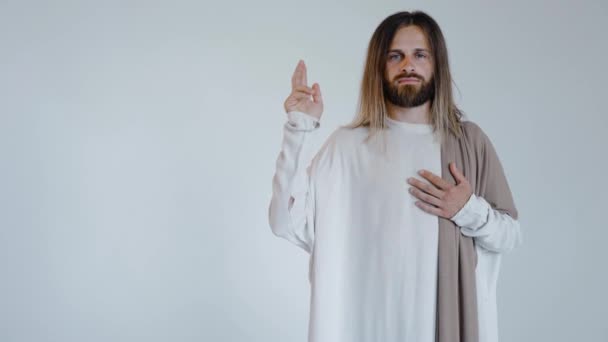 Jesús con la mano levantada mira a la cámara sobre un fondo blanco. Estudio. — Vídeos de Stock