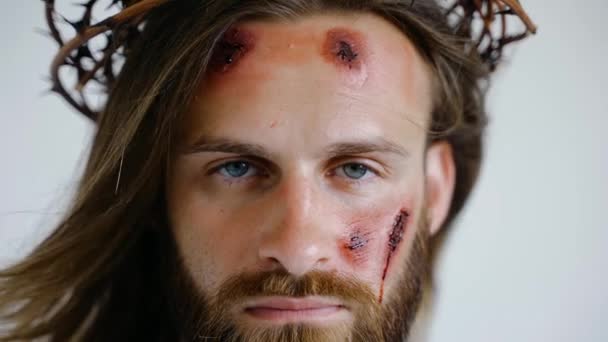 Jesus in a crown of thorns with wounds on face looks into the camera. Close up — Stock Video