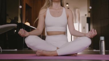  Genç sarışın kadın yoga minderinde oturuyor meditasyon pozunda gözleri kapalı.