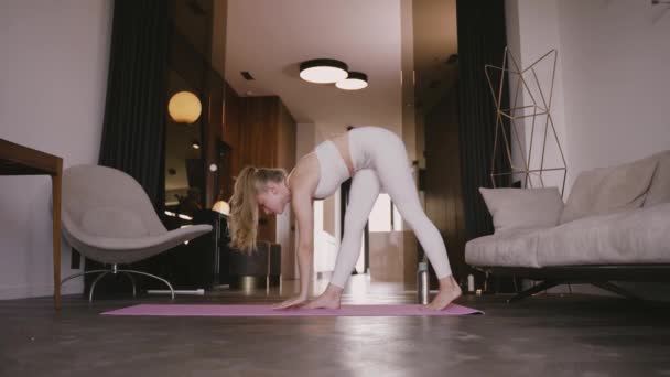 Ung blond kvinna som står på yogamattan och stretchar — Stockvideo