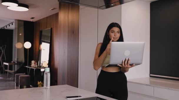 En ung mörkhyad brunett med laptop i händerna går genom köket — Stockvideo