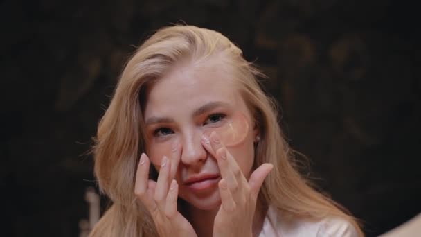 Młoda blondynka w białym szlafroku w łazience używa łatek pod oczami — Wideo stockowe