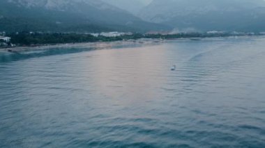 Mavi denizde tekne yelken açar. Gün batımında dağlar yukarıdan. Güzel manzara..