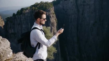 Güneş gözlüklü bir gezgin dağın tepesinde durur ve pusulaya bakar.