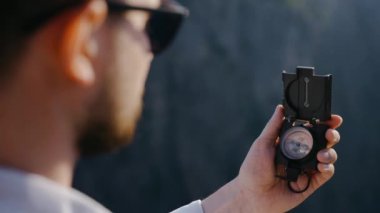 Güneş gözlüklü bir gezgin dağın tepesinde durur ve pusulaya bakar.