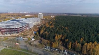 Şehrin kenar mahallelerinde bir alışveriş merkezi ve metal ve betondan yapılmış endüstriyel bir bina inşa edilişinin havadan görüntüsü. Sonbahar güneşli bir gün. Ağaçlardaki yapraklar sararır