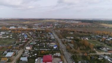 Büyük köyün havadan görünüşü. Ana cadde boyunca çok sayıda araba sürüyor. Yol tamiri nedeniyle trafik sıkışık. Yakınlarda küçük bir gölet var. Köyde sarı yapraklı birçok ağaç var. Sonbahar güneşli bir gün.