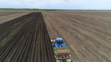Baharda çiftliğin geniş tarlasında patates yetiştirmek için kullanılan bir makineyle mavi bir traktörün hava görüntüsü..