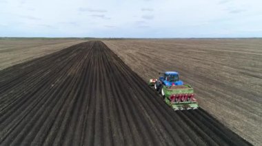 Baharda çiftliğin geniş tarlasında patates yetiştirmek için kullanılan bir makineyle mavi bir traktörün hava görüntüsü..