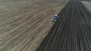 Baharda çiftliğin geniş tarlasında patates yetiştirmek için kullanılan bir makineyle mavi bir traktörün hava görüntüsü..