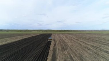 Baharda çiftliğin geniş tarlasında patates yetiştirmek için kullanılan bir makineyle mavi bir traktörün hava görüntüsü..