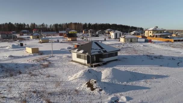 冬のコテージ村の建設中の近代的な家の空中ビュー 家の近くには未舗装の雪道や粘土の山があります 建設のための無料の地面があります — ストック動画